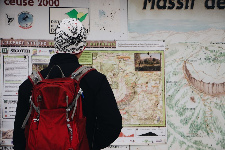 Pessoa de mochila estudando um mapa de trilhas diante das montanhas